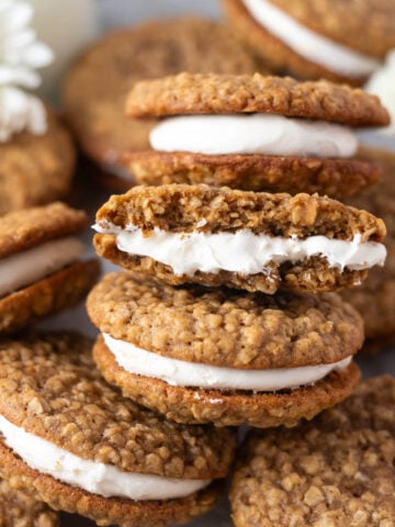 pile of oatmeal cream pie cookies on a parchment lined baking sheet with milk and white flowers in the background