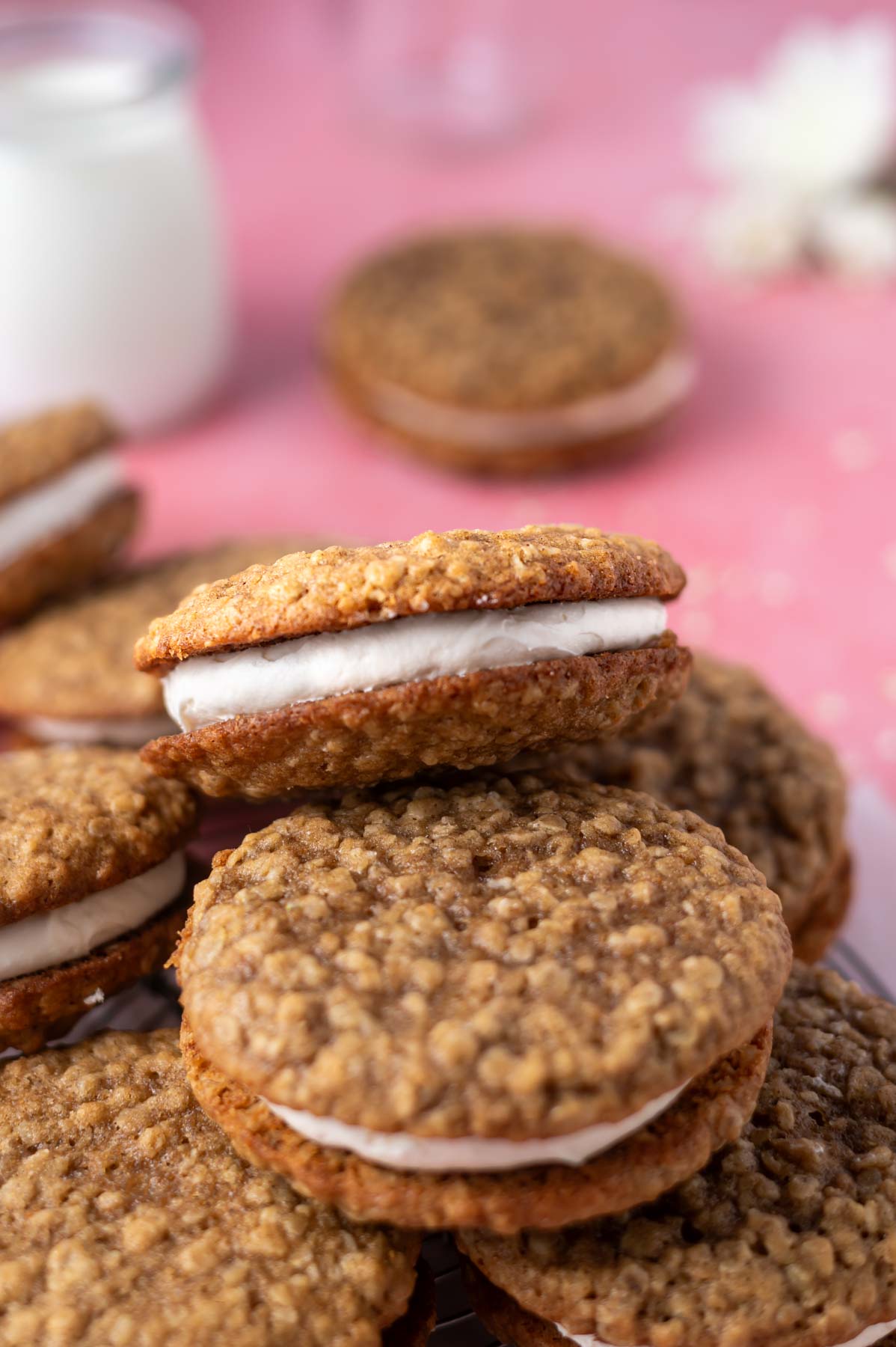 oatmeal cream pie cookie on it's side in a pile showing the filling with milk in the background