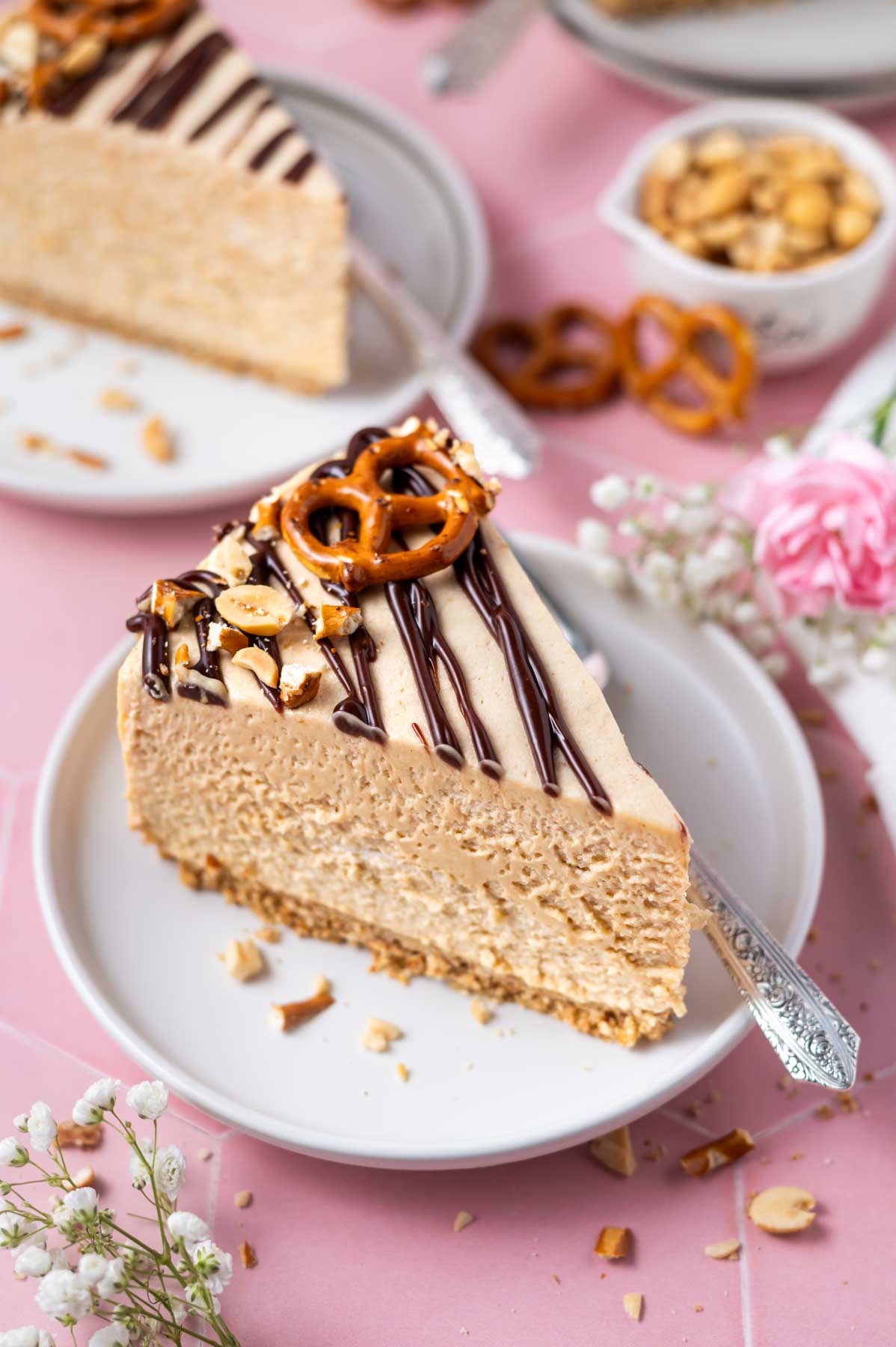 slice of peanut butter pretzel pie on a plate with a fork and a bowl of peanuts and fresh flowers in the background