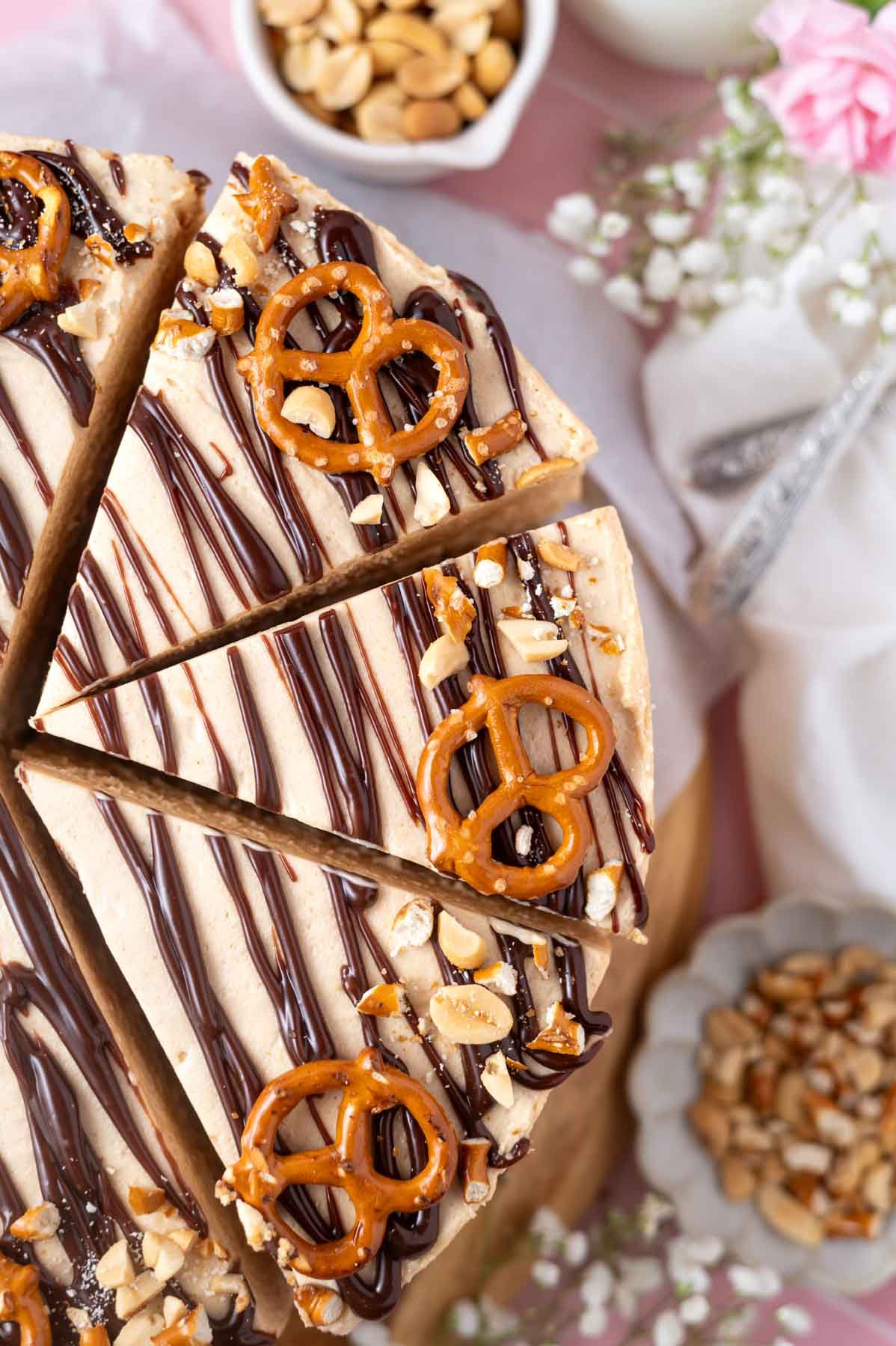 cut slices of peanut butter pretzel pie on a cake stand with flower and utensils in the background