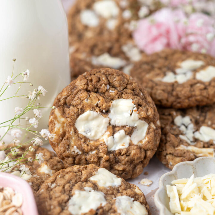 brown butter oatmeal cookie leaned up against a glass of milk with fresh flowers in the background