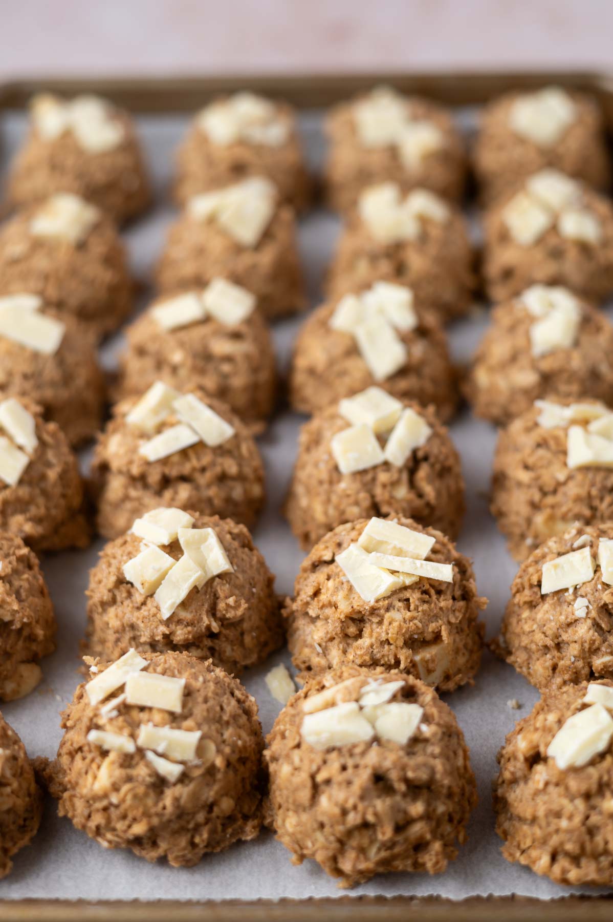 cookie dough balls with white chocolate on top on a parchment lined baking sheet