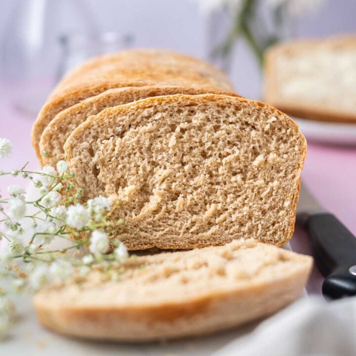 slices of homemade sandwich bread on a board with a knife and fresh flowers
