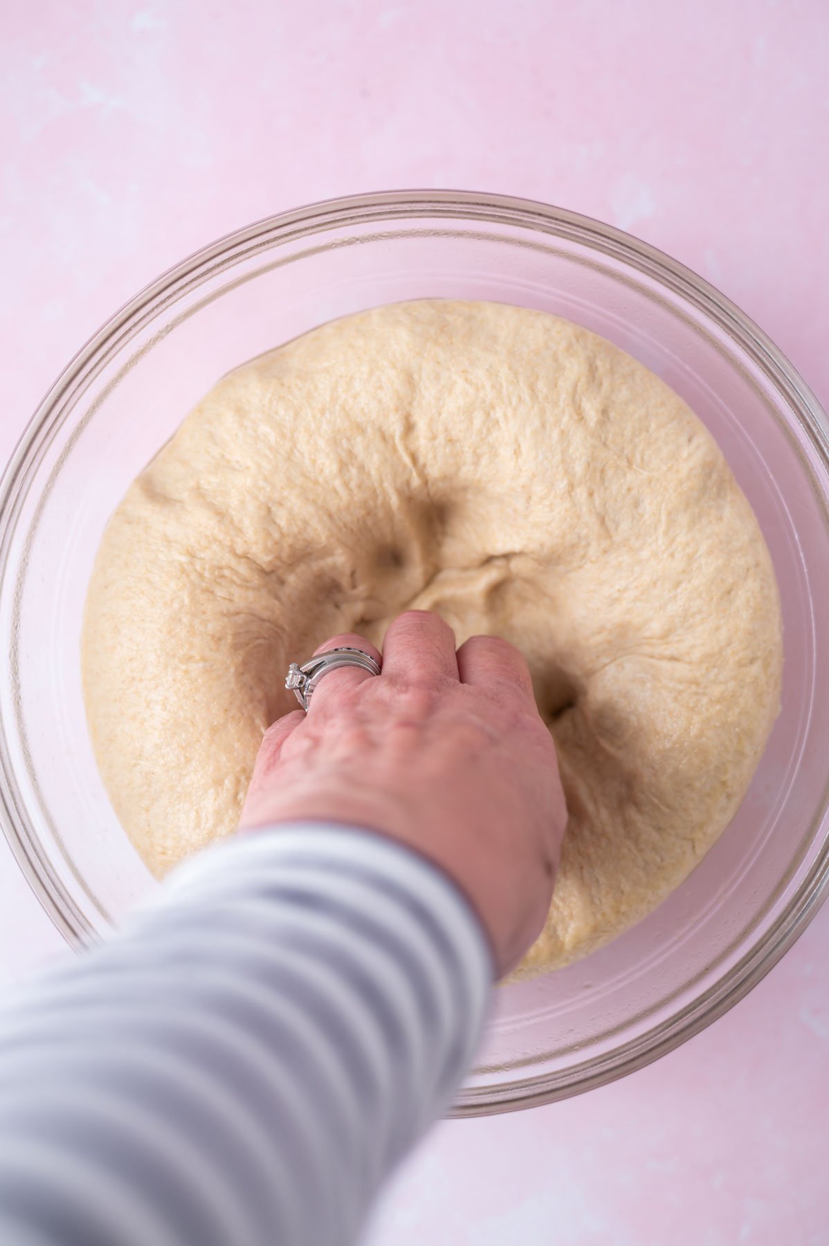 hand pressing the air out of bread dough in a bowl