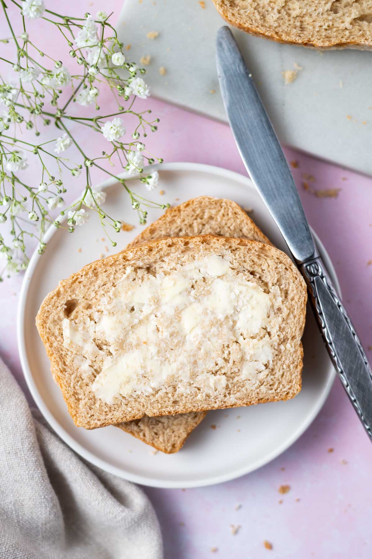 slices of whole wheat sandwich bread on a plate with butter and a knife