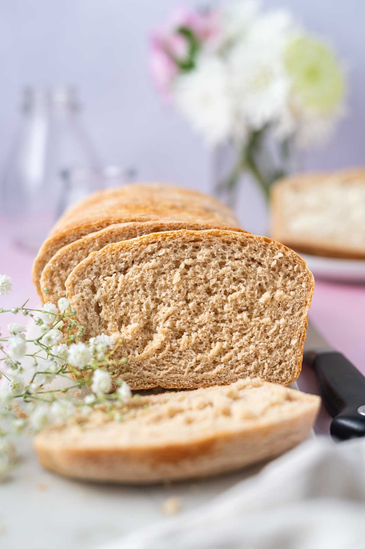 slices of homemade sandwich bread on a board with a knife and fresh flowers