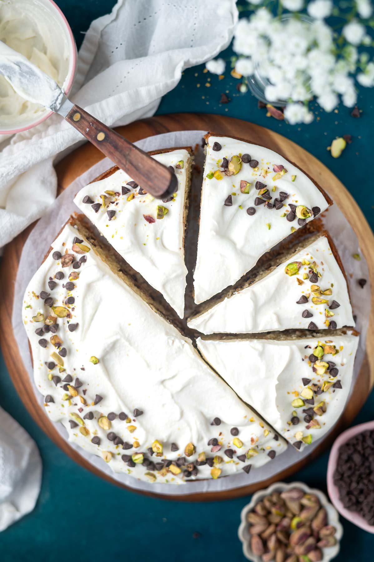 overhead look at sliced cake on a plate with a napkin and bowls of mini chocolate chips and pistachios