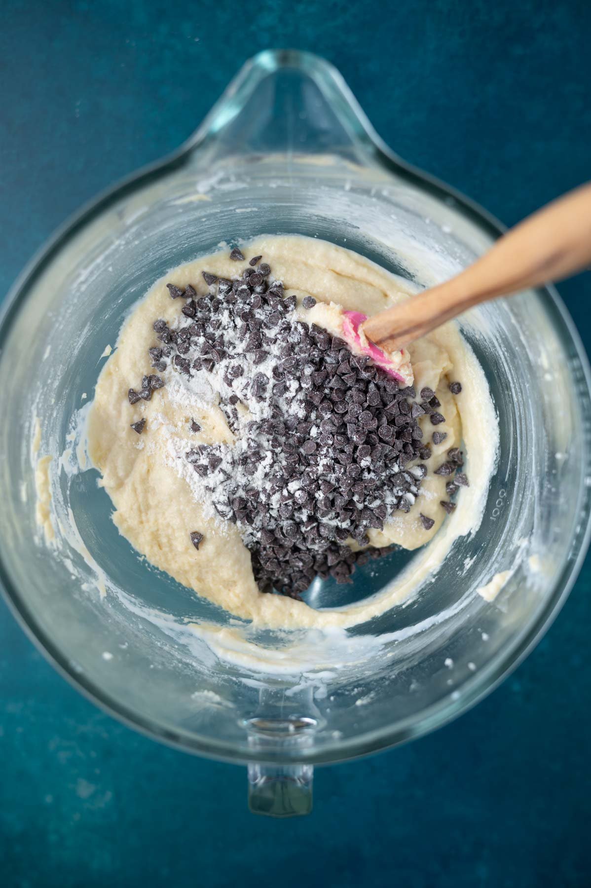 mini chocolate chips being added to cake batter in a bowl with a spatula