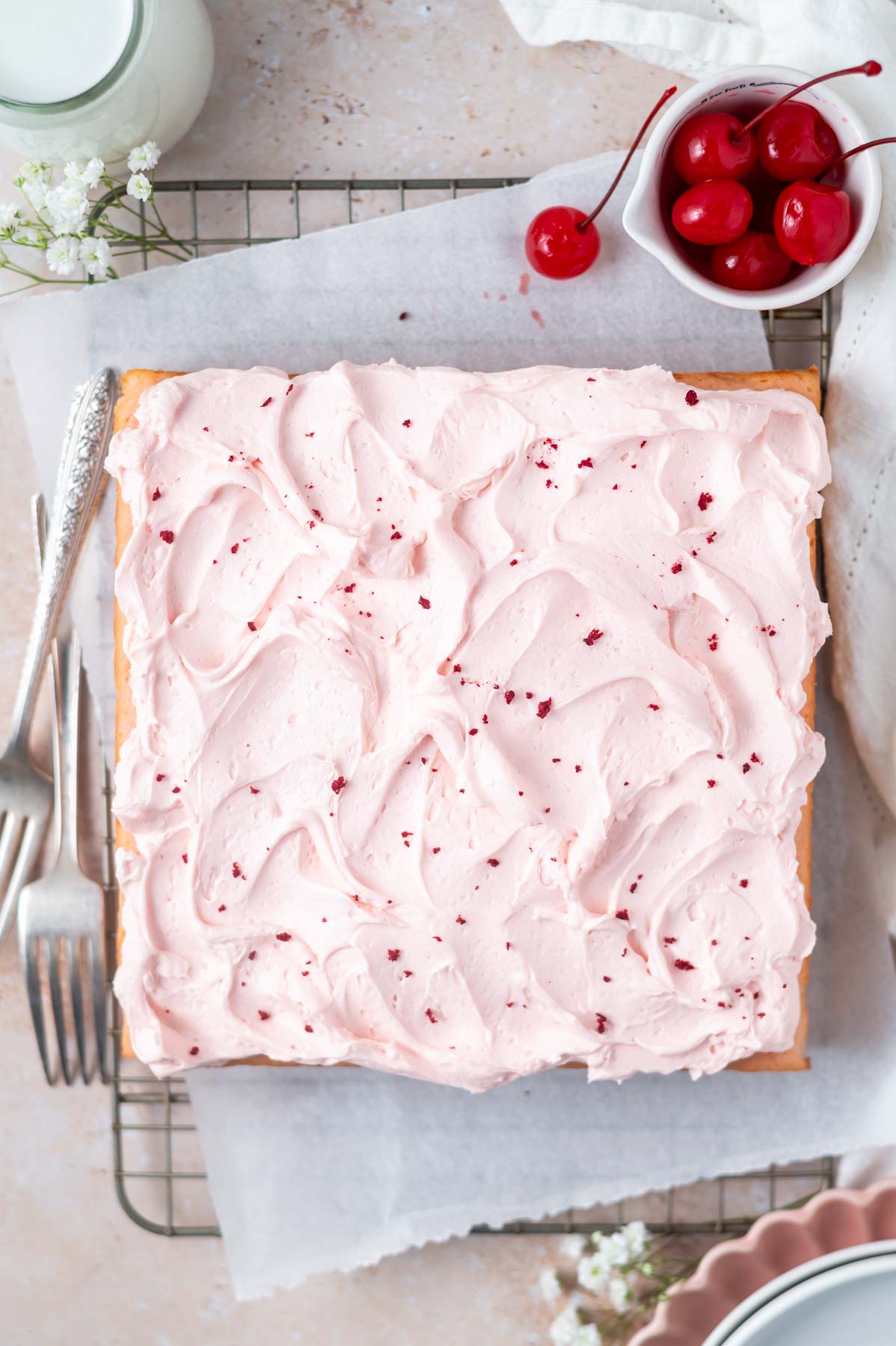 decorated cake on a parchment lined cooling rack with forks and a bowl of cherries