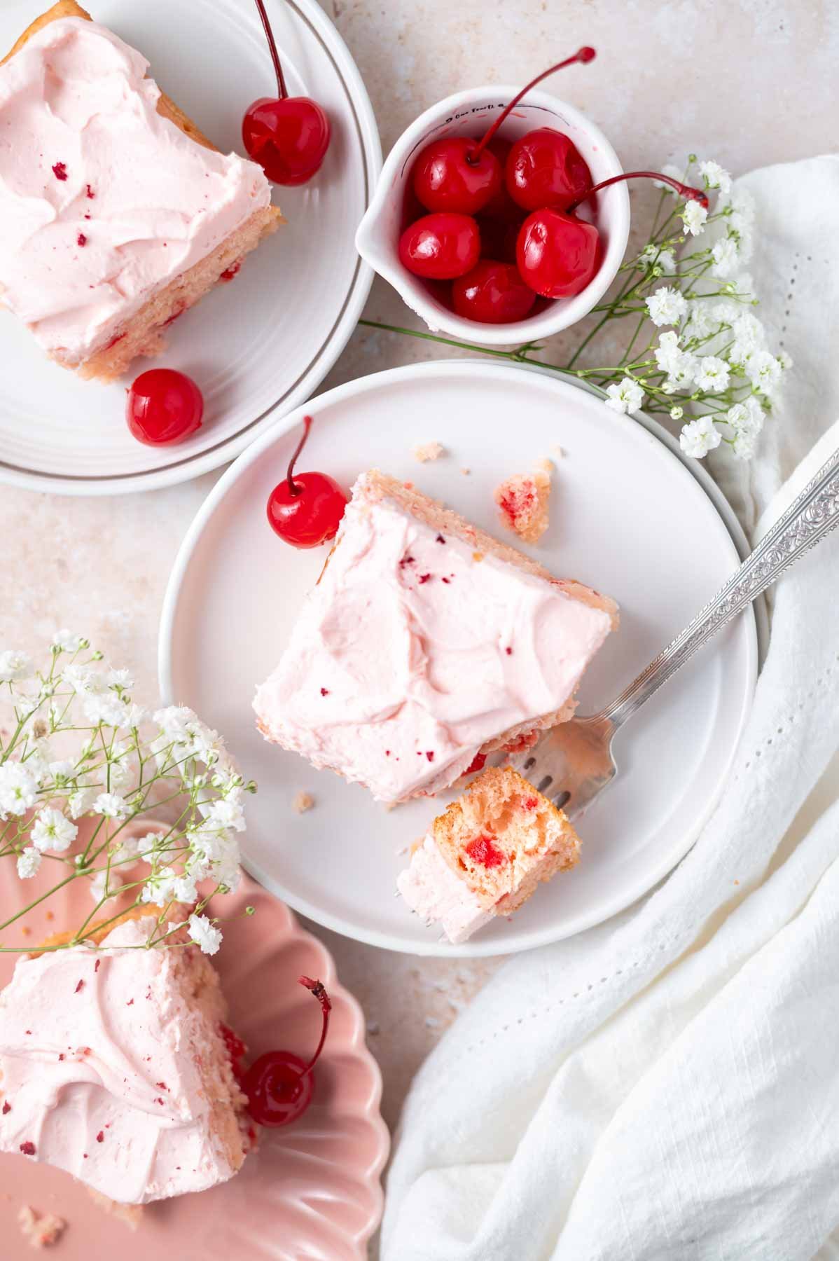 slices of cherry chip cake on a plates with a bite on a fork and a bowl of cherries