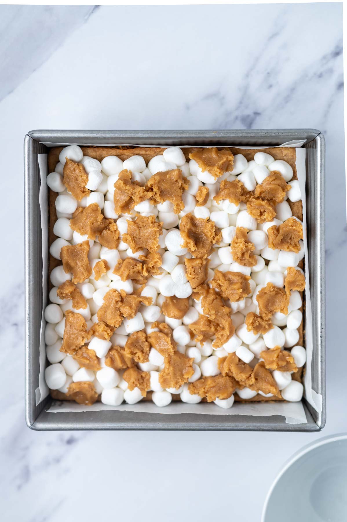 extra peanut butter dough crumbled over top of marshmallows in a baking pan