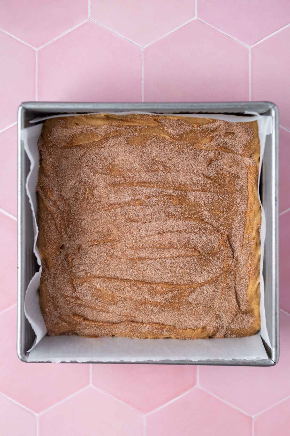 cinnamon and sugar sprinkled over dough in a parchment lined pan