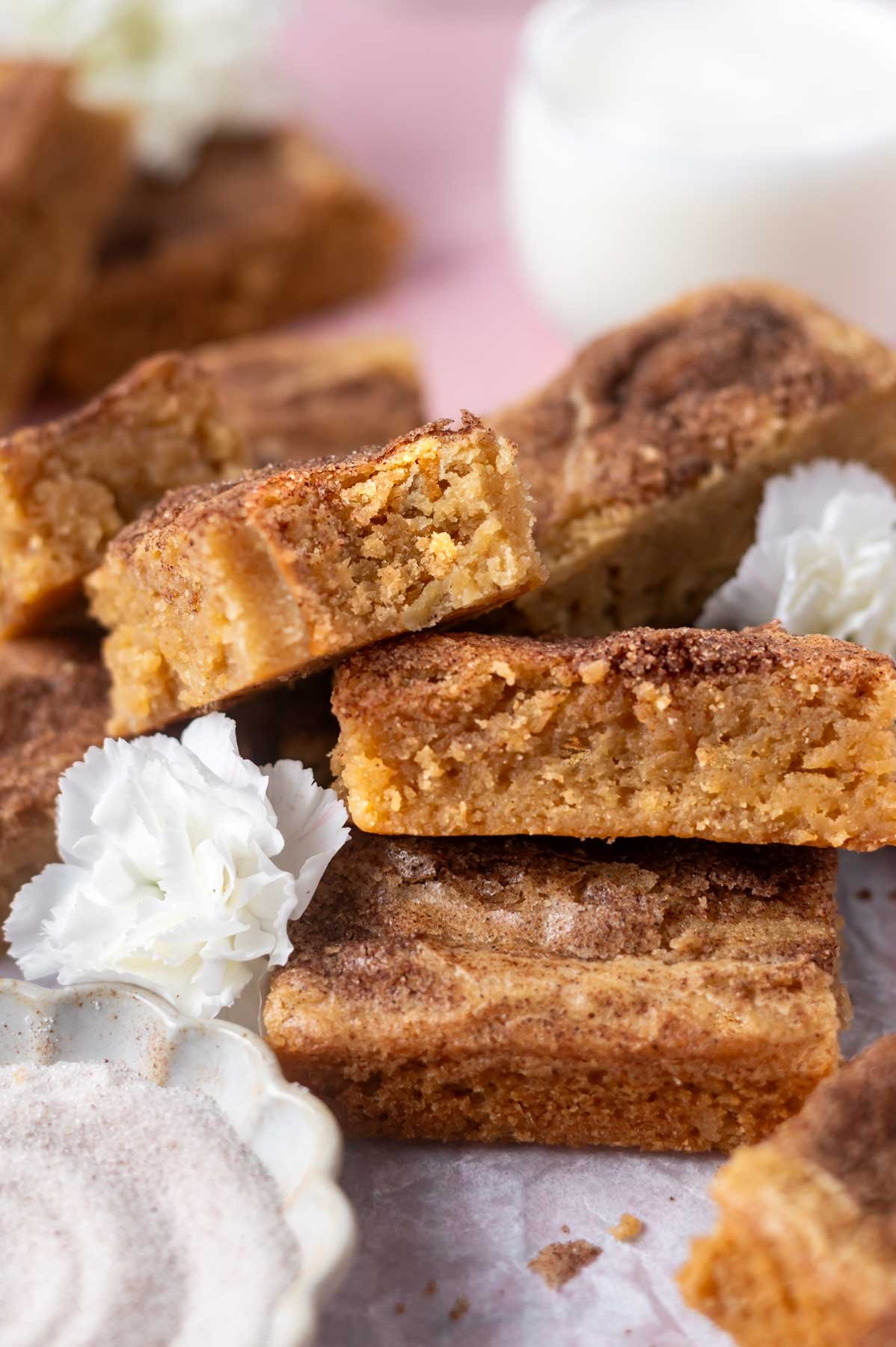 pile of snickerdoodle cookie bars with a glass of milk and a bowl of cinnamon sugar