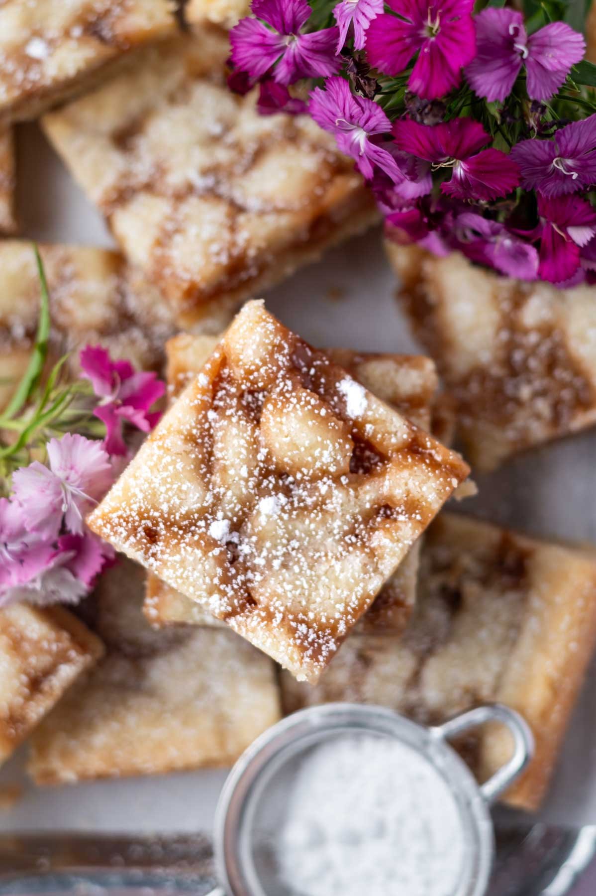 overhead look at caramel cookie bars with confectioners' sugar dusted over the top and fresh pink flowers