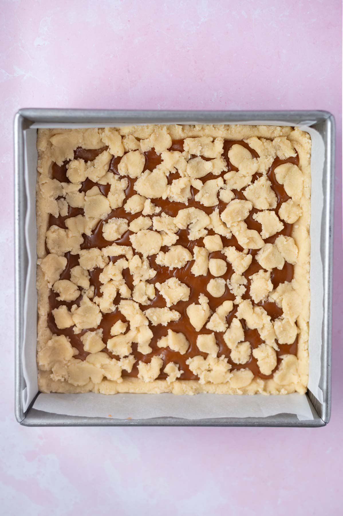 cookie dough crumbled over caramel in a baking tin