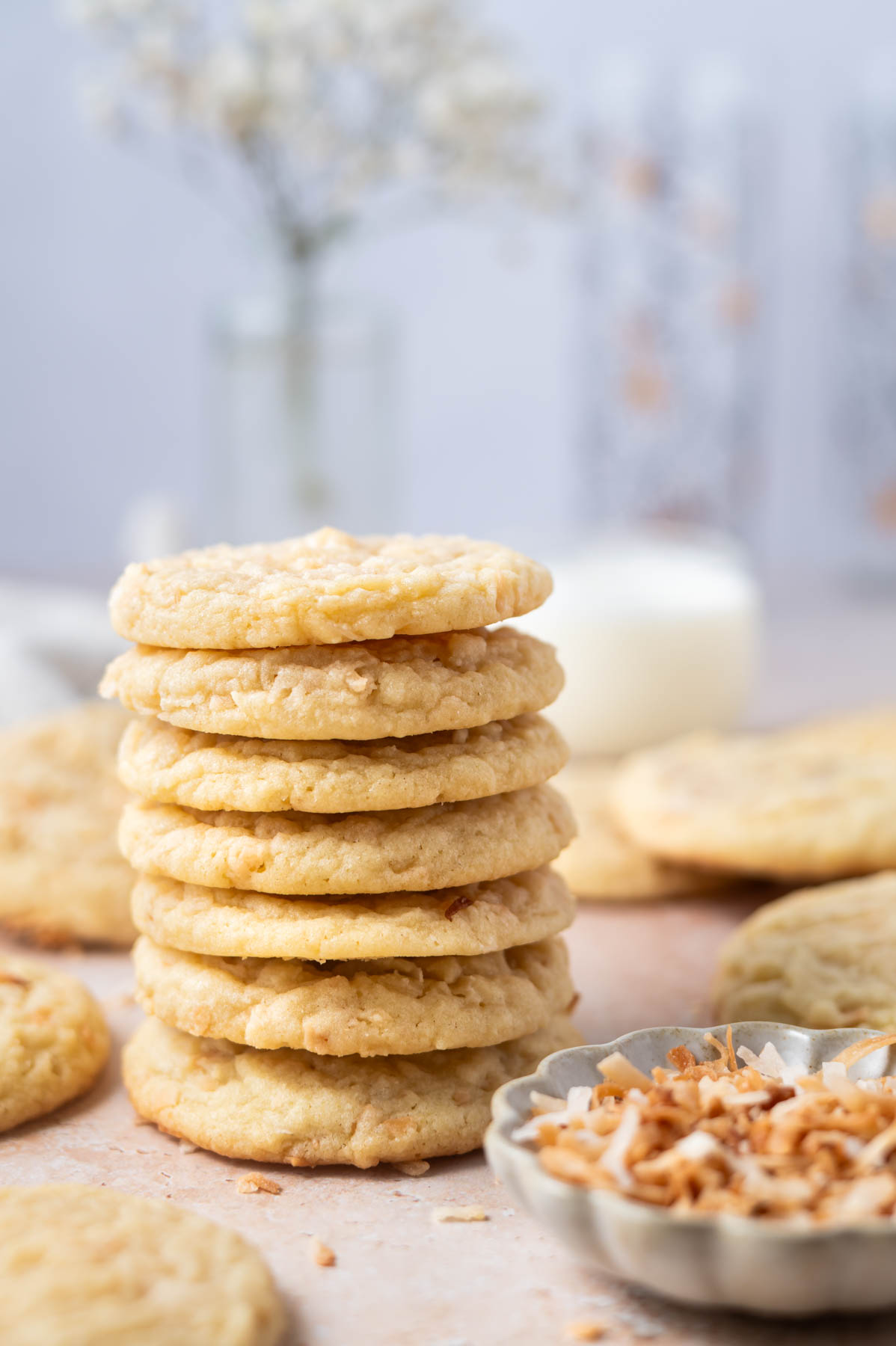 stack of cookies with milk in the background and a bowl of coconut