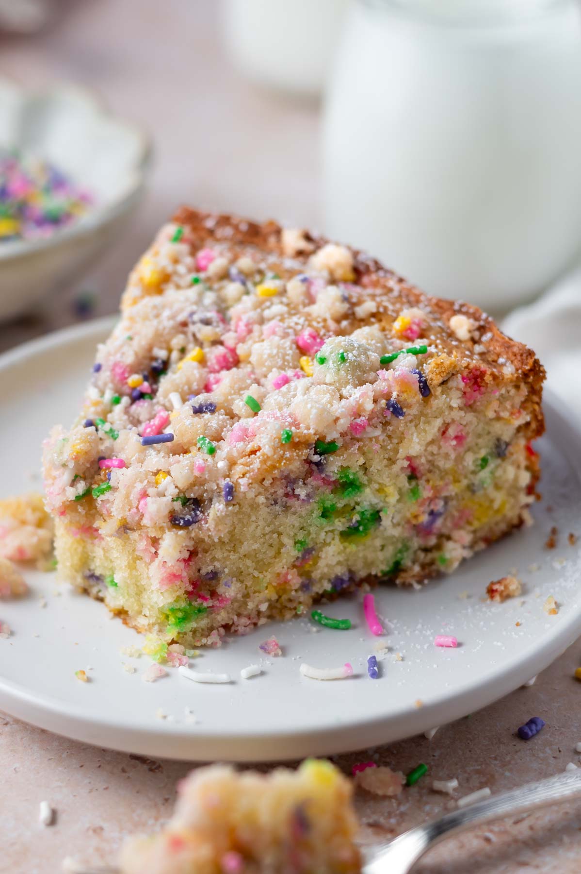 slice of sprinkle cake on a plate with milk in the background