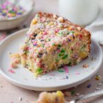 slice of sprinkle cake on a plate with milk in the background