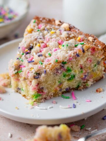 slice of sprinkle cake on a plate with milk in the background