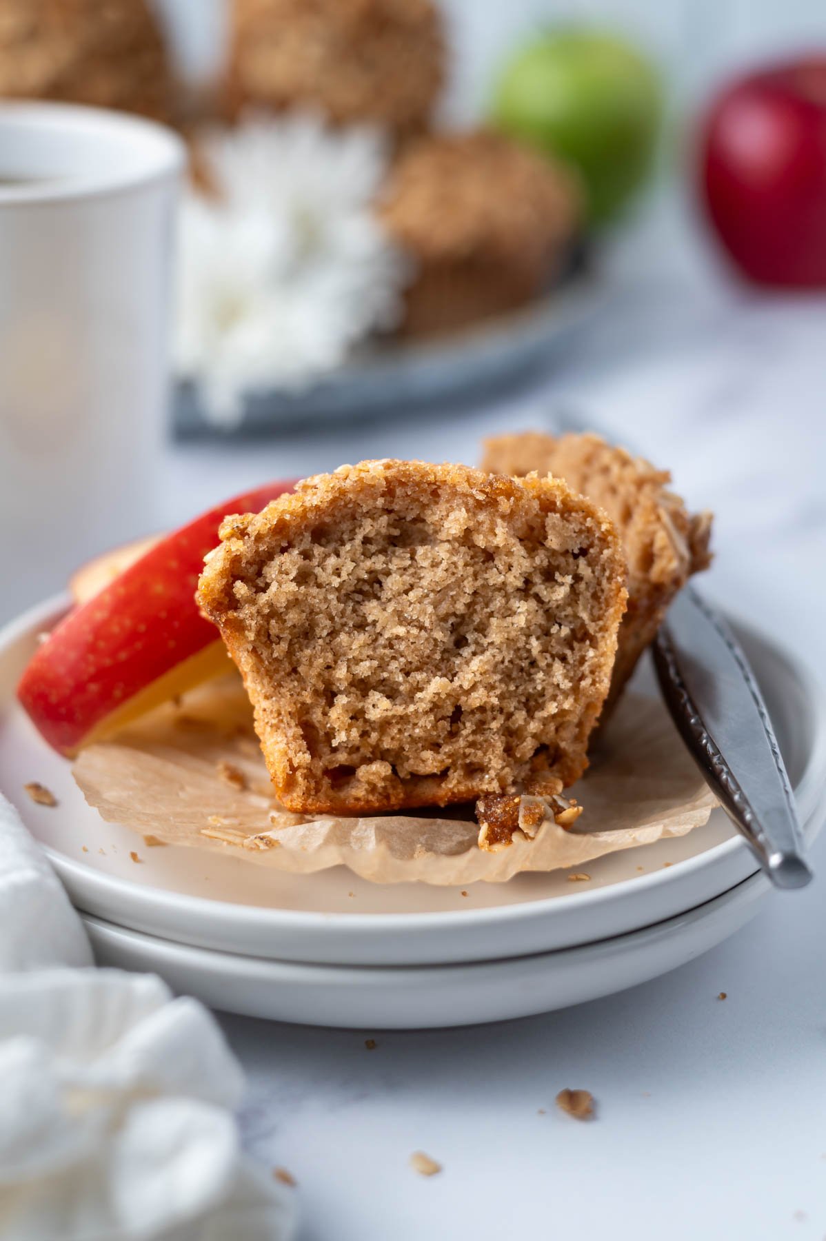 muffin split in half showing moist crumb on a plate with a knife and apple slices