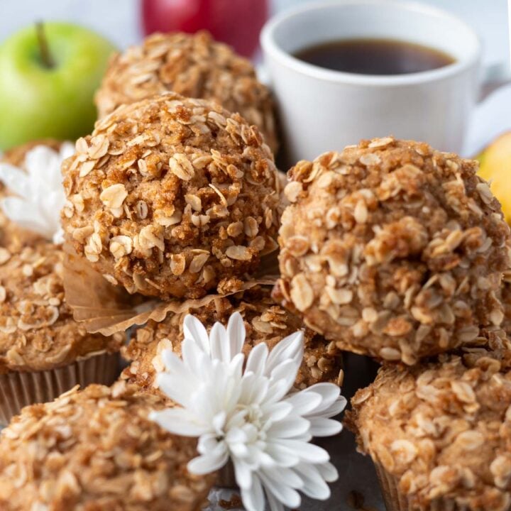 apple cider muffins with streusel on a tray with fresh flours and a cup of coffee