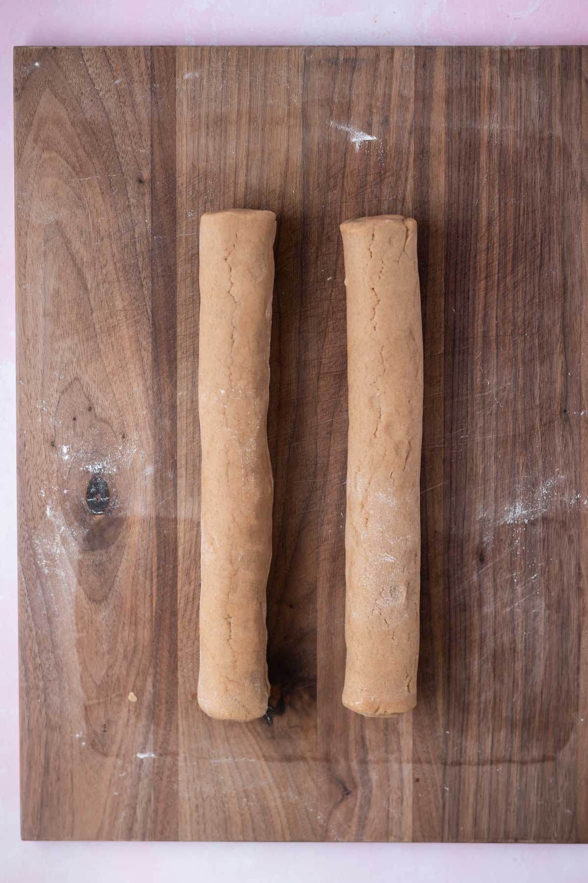 two rolled logs of cookie dough on a cutting board