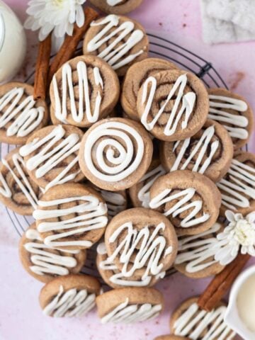pile of cinnamon roll sugar cookies on a cooling rack with a glass of milk
