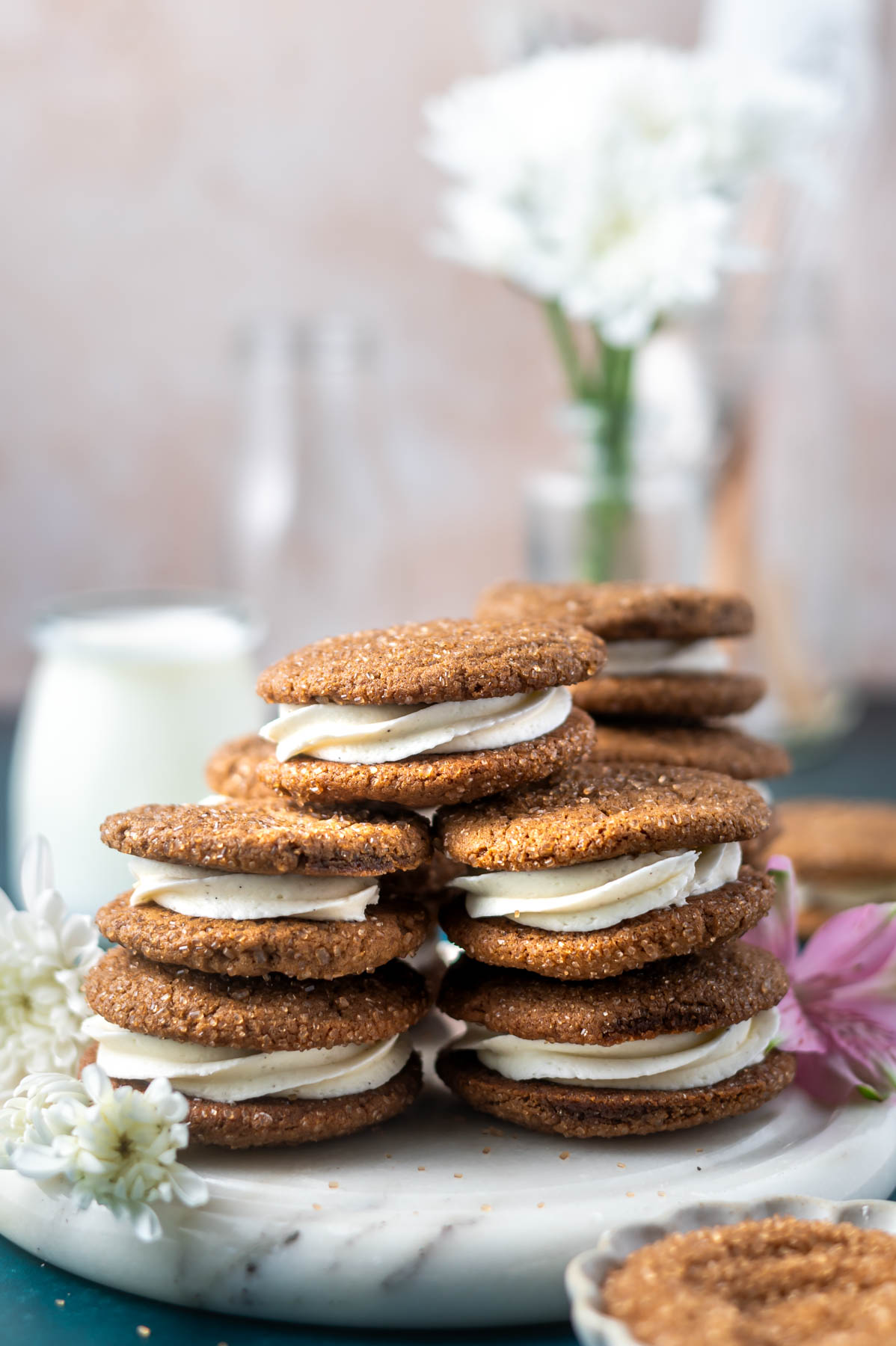 stacks of cookies on a marble tray with flowers and milk in the background