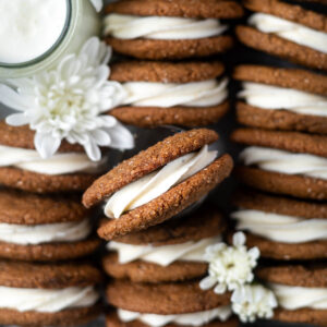 overhead look at gingerbread sandwich cookies in a tray with a glass of milk and fresh white flowers