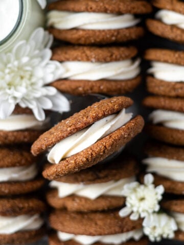 overhead look at gingerbread sandwich cookies in a tray with a glass of milk and fresh white flowers