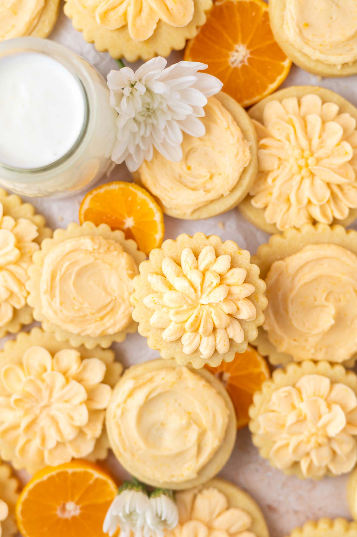 overhead look at decorated cookies on parchment paper with orange slices and a glass of milk