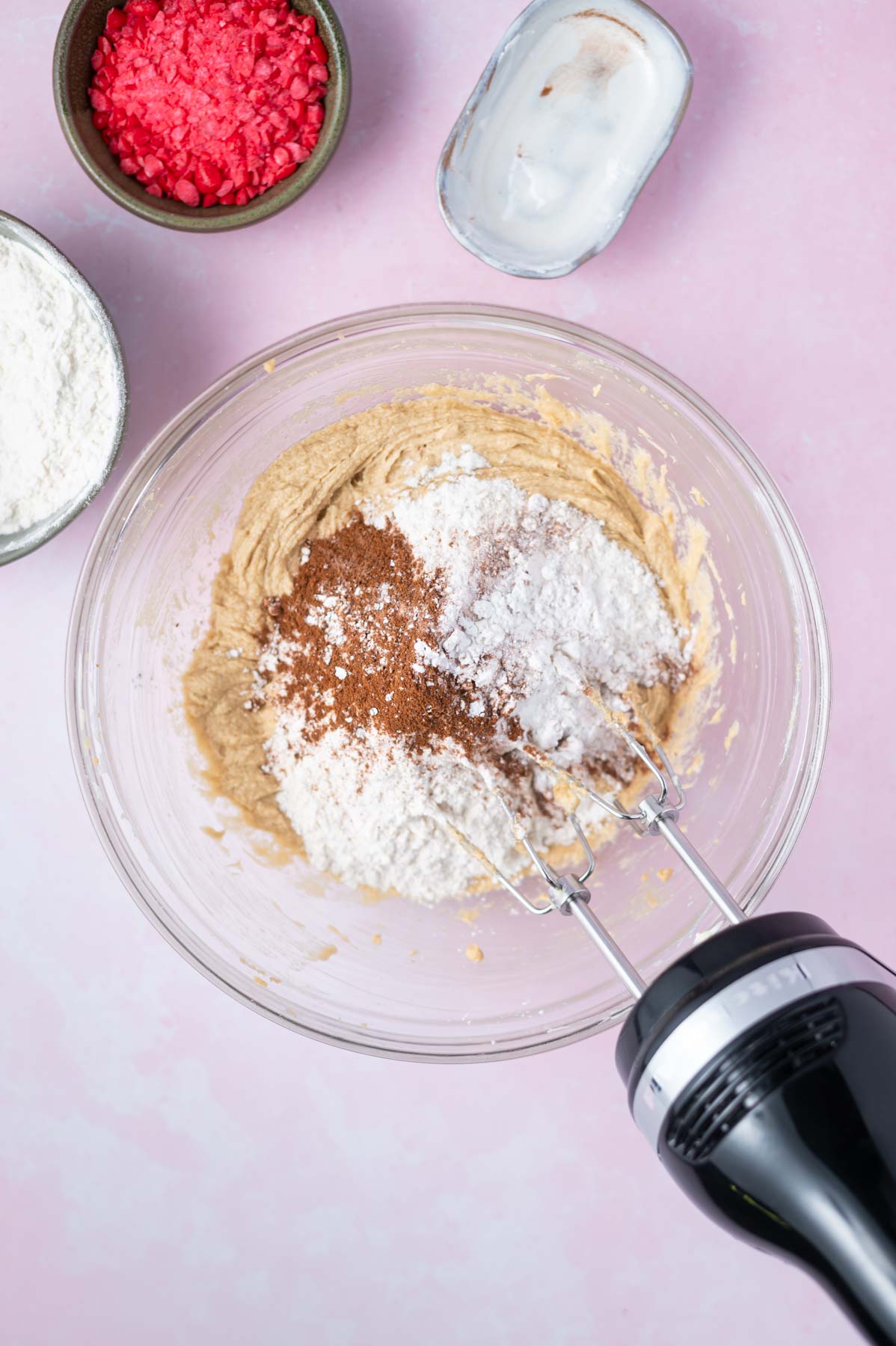 dry ingredients added to dough in a mixing bowl with a hand mixer