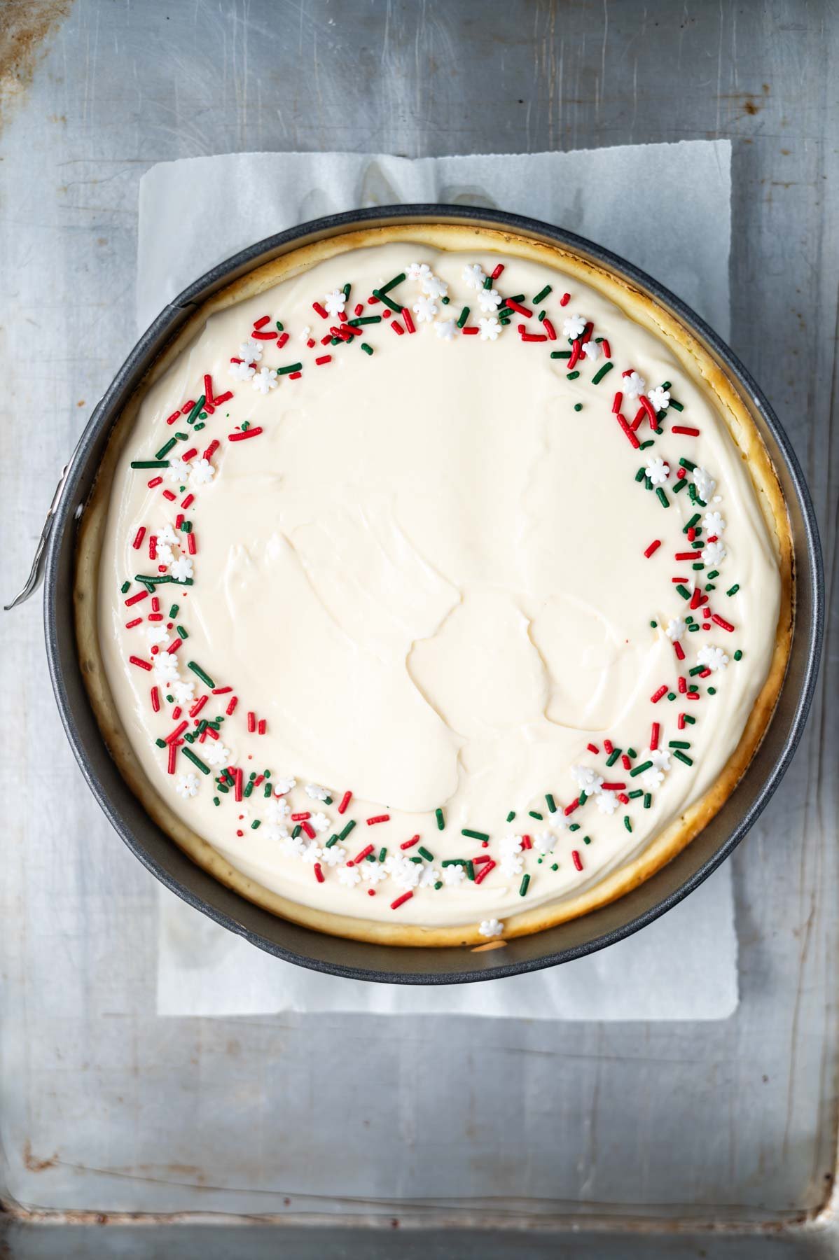 cheesecake with sprinkle decorations sitting on a baking sheet pan
