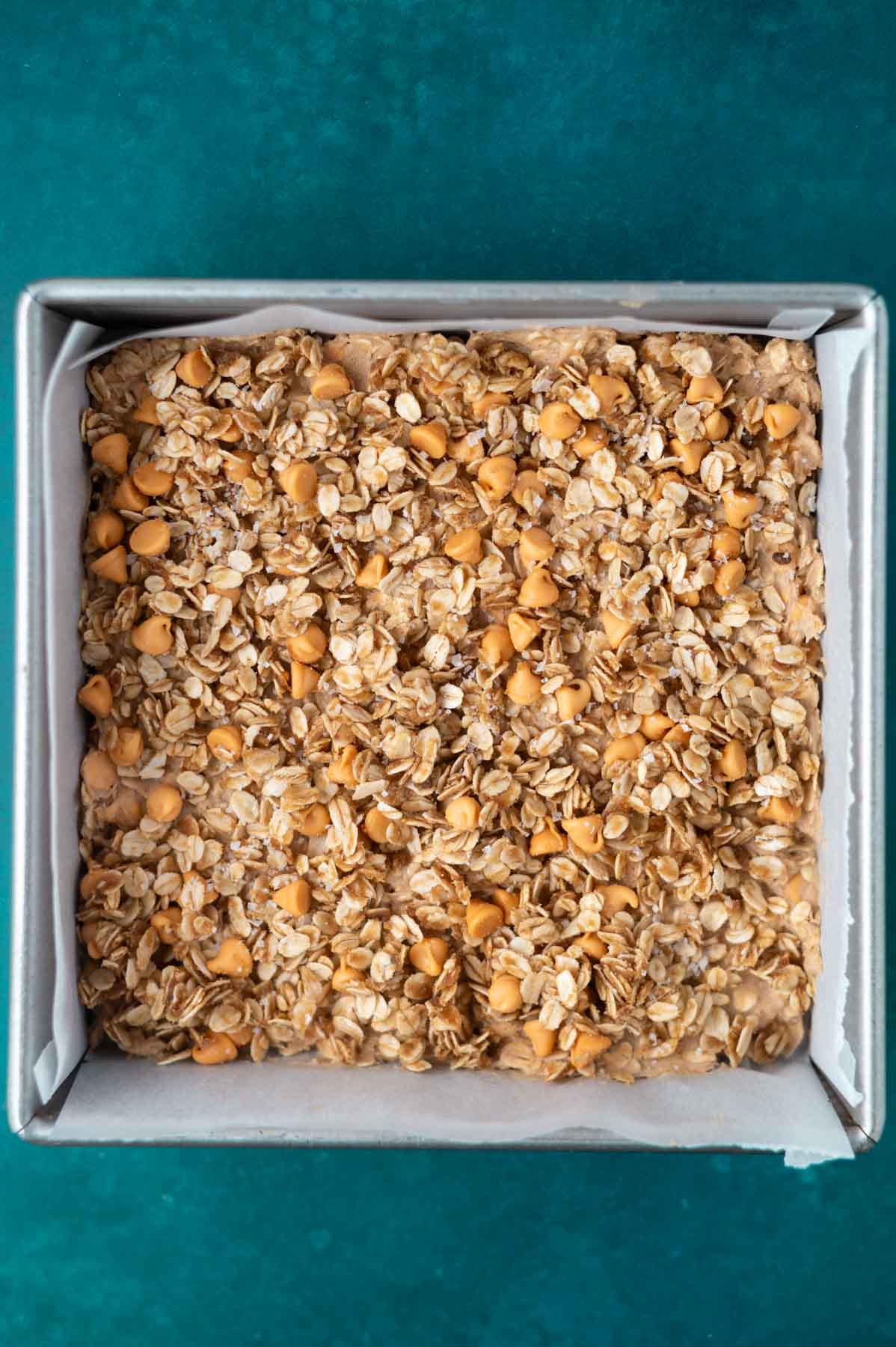 streusel added to cookie bar dough in a parchment lined baking pan