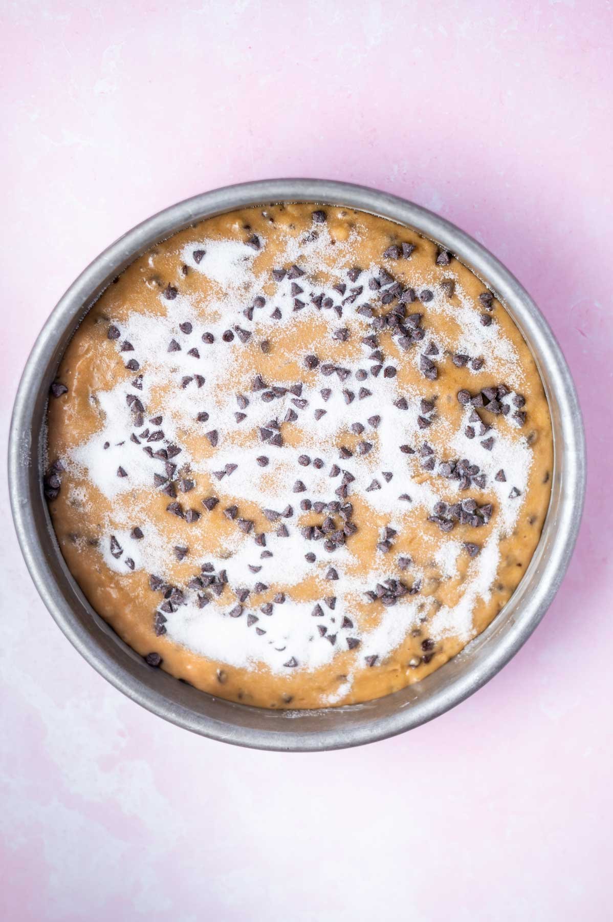 cake batter in a round baking pan with chocolate chips and sugar sprinkled over the top