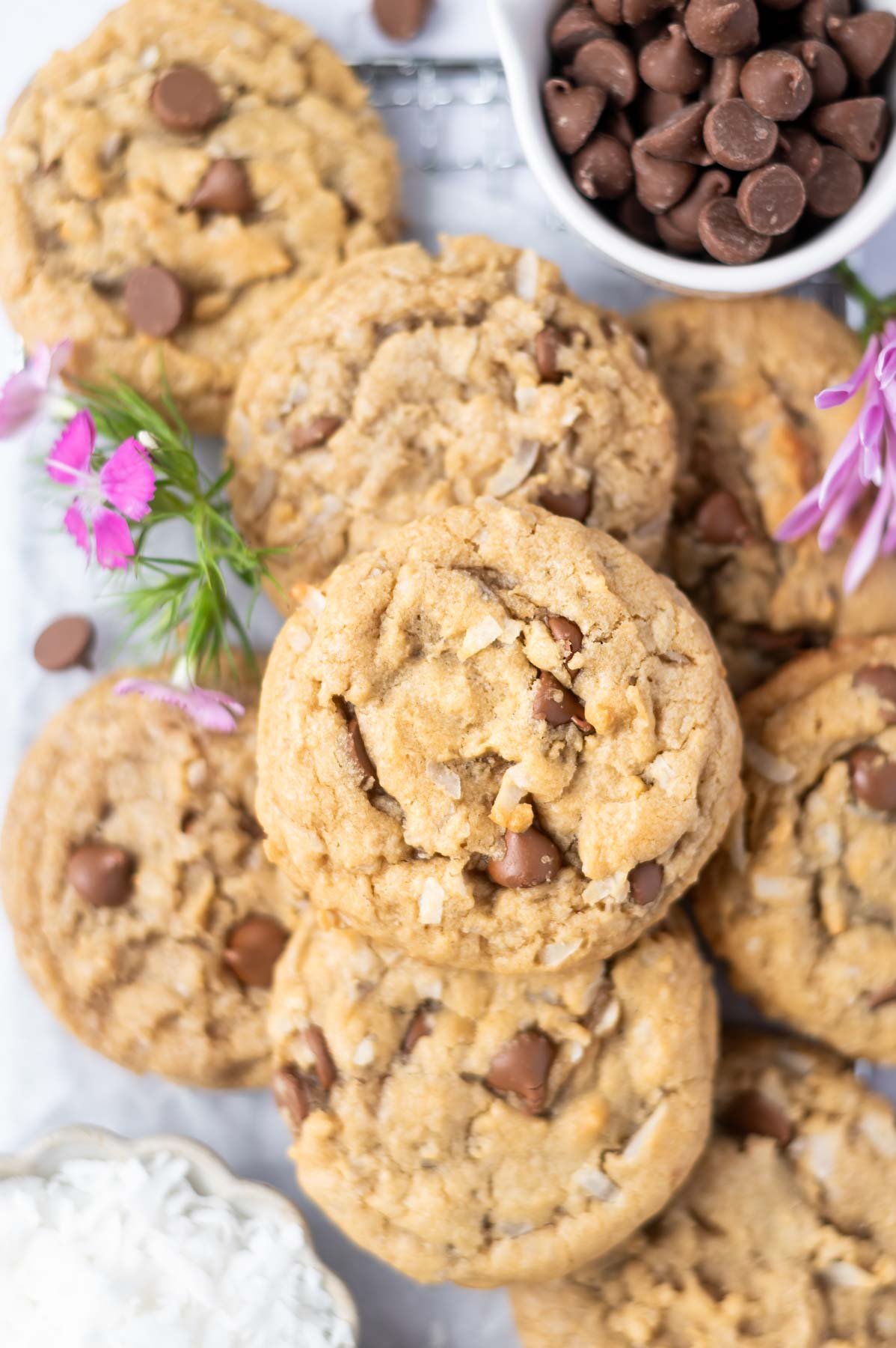 cookies on a cooling rack with bowl of chocolate chips and coconut