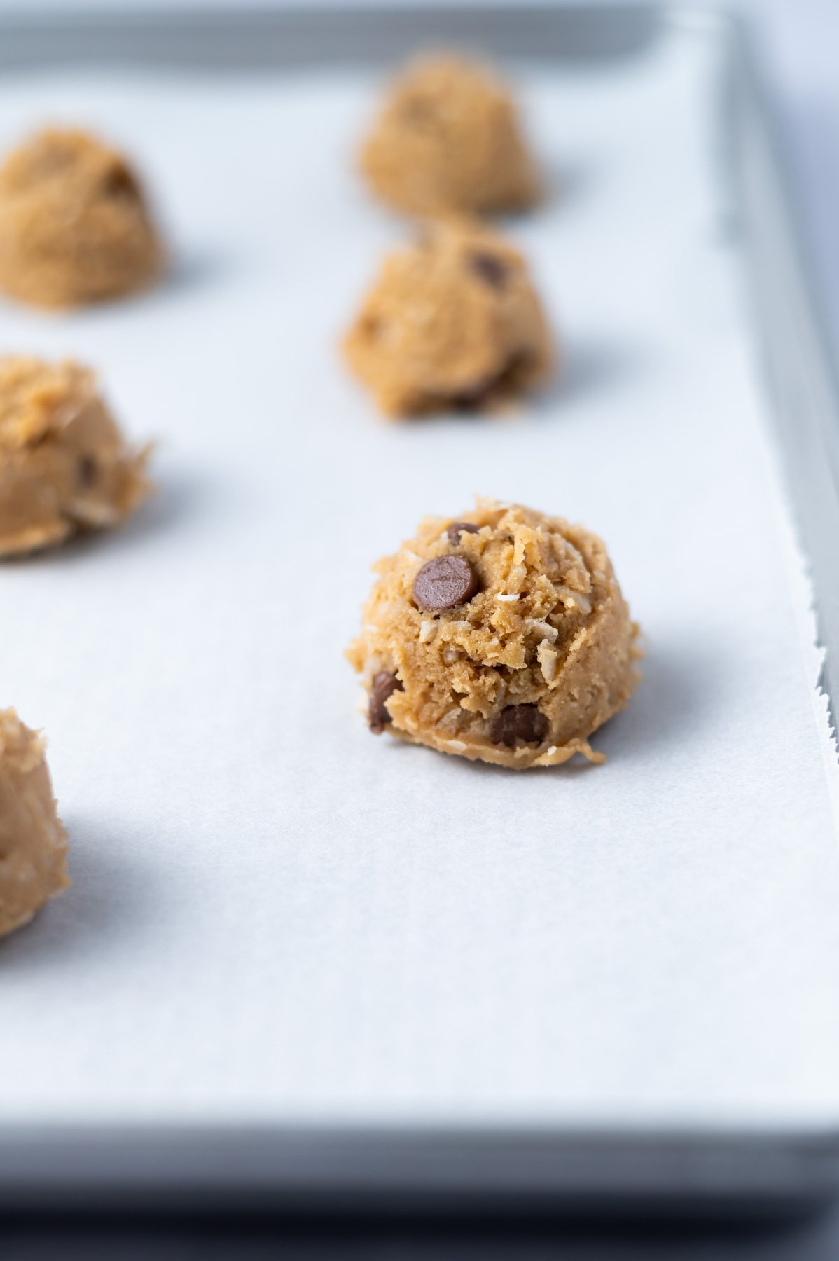 coconut chocolate chip cookie dough balls on a parchment lined baking sheet