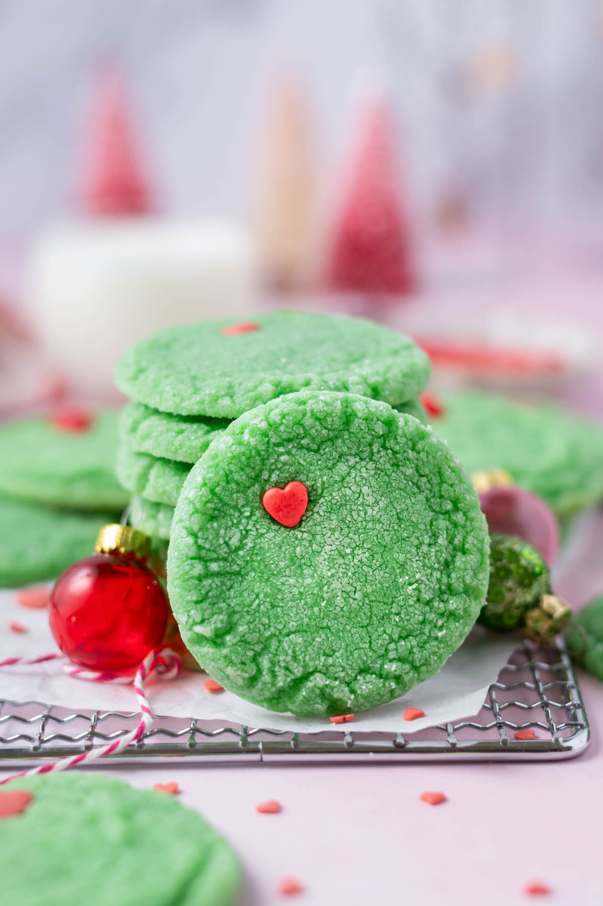 grinch cookie leaning up against a stack of cookies with milk and Christmas trees in the background