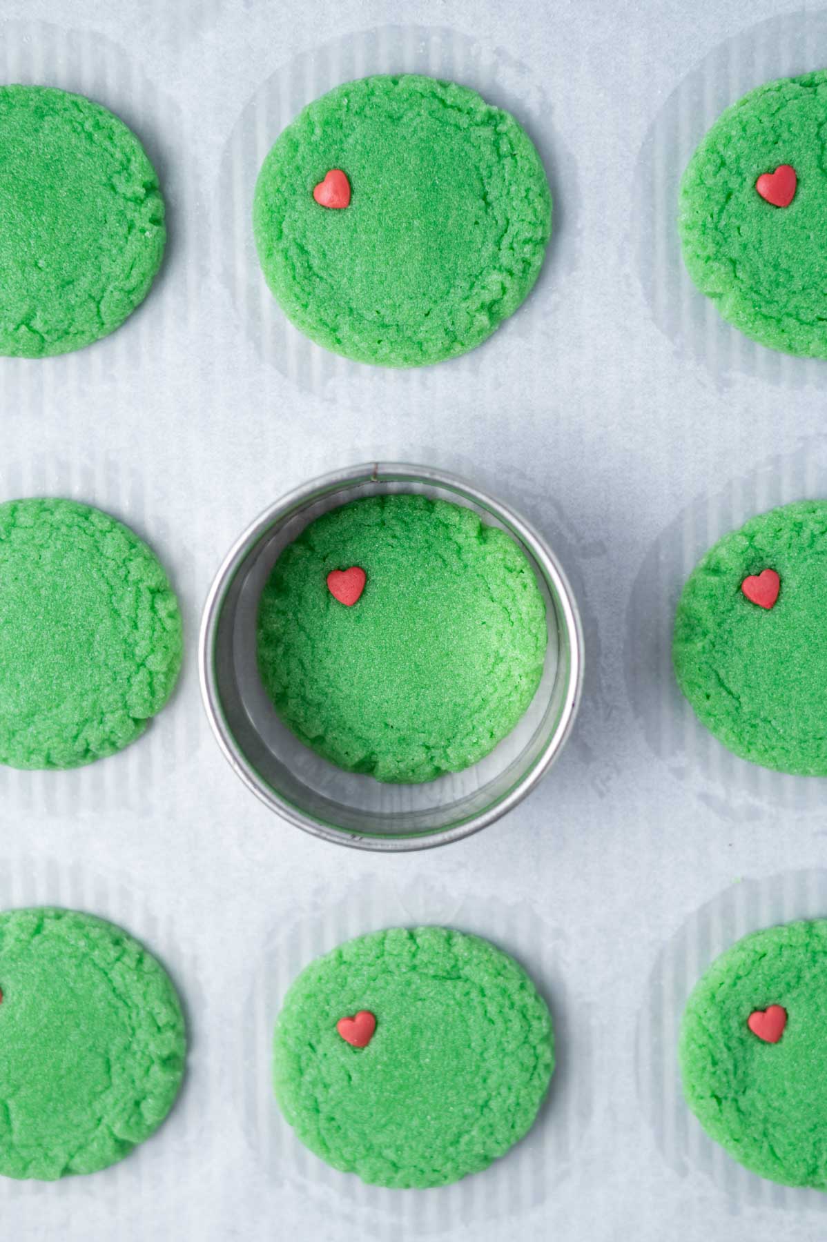 round green baked cookies on a parchment lined baking sheet with a biscuit cutter around one
