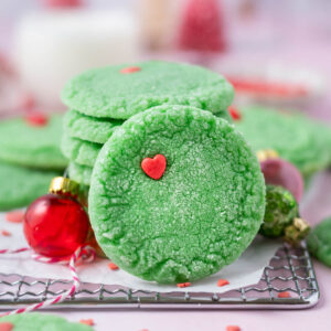 grinch cookie leaning up against a stack of cookies with milk in the background