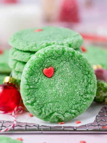 grinch cookie leaning up against a stack of cookies with milk in the background
