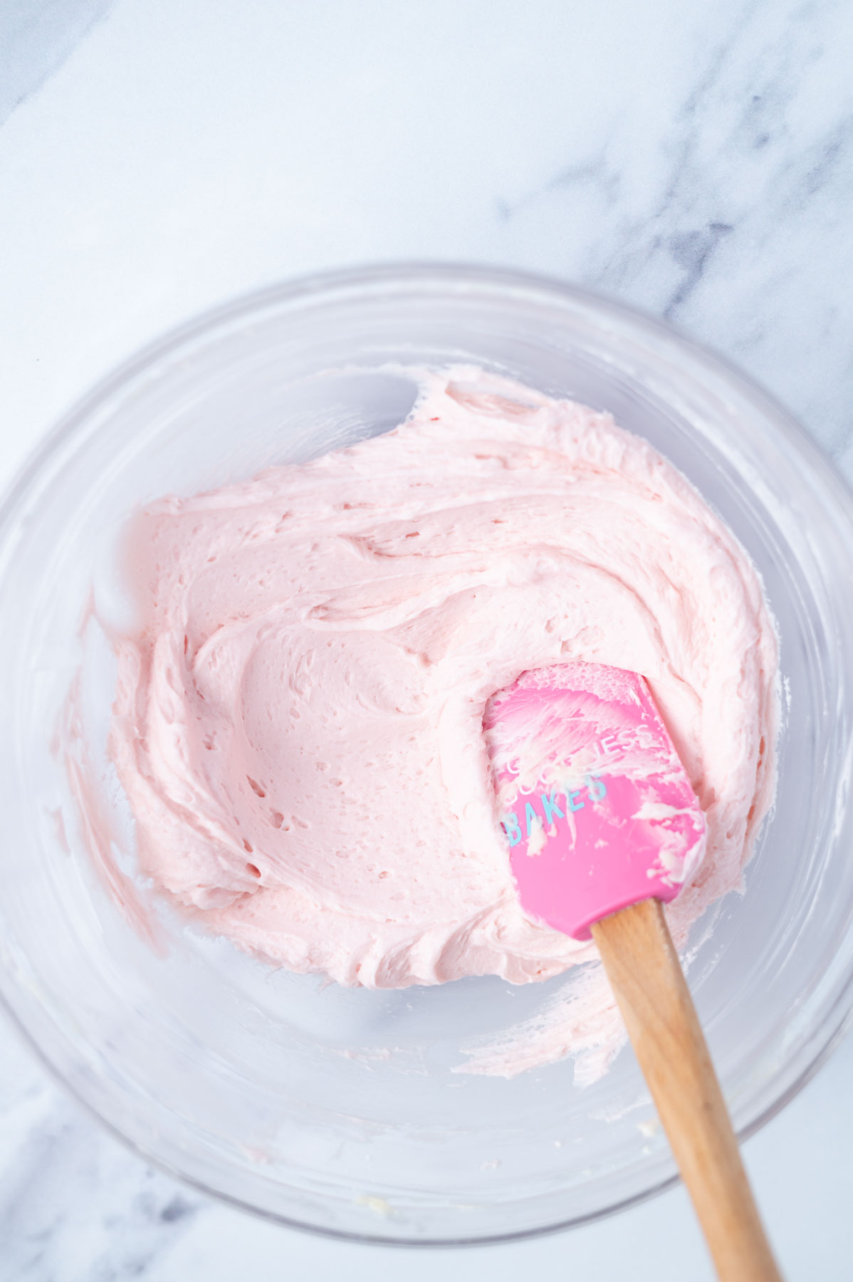 pink buttercream in a mixing bowl with a pink spatula