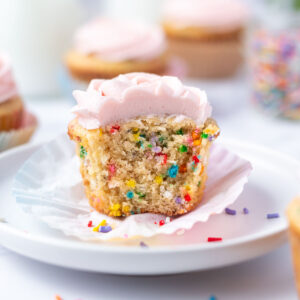 birthday cupcake with a bite missing sitting on a plate with more cupcakes and milk in the background