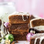 stack of gingerbread blondies with white chocolate drizzle, a cup of milk and Christmas ornaments