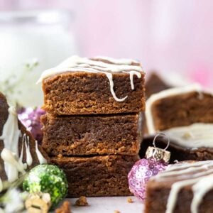 stack of gingerbread blondies with white chocolate drizzle, a cup of milk and Christmas ornaments