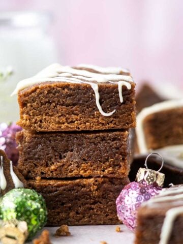 stack of gingerbread blondies with white chocolate drizzle, a cup of milk and Christmas ornaments