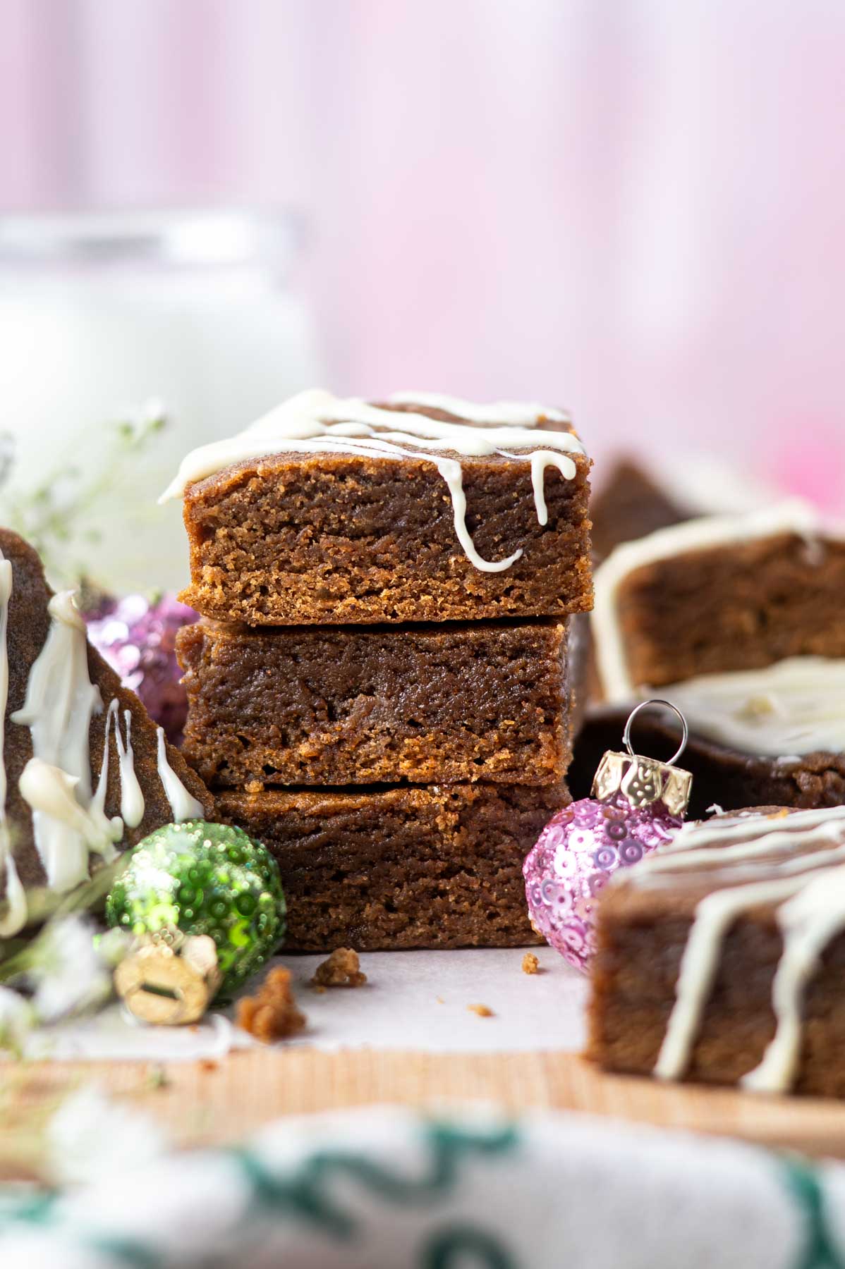 stack of gingerbread blondies with white chocolate drizzle, a cup of milk and Christmas ornaments