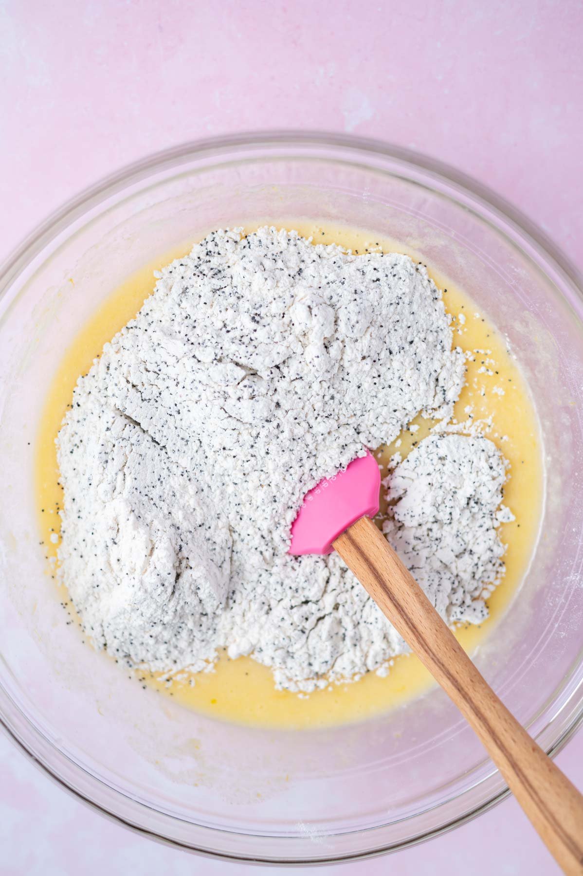 flour and poppy seeds added to batter in a bowl with a spatula