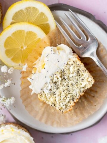 half lemon poppy seed cupcake on a plate with a fork and lemon slices