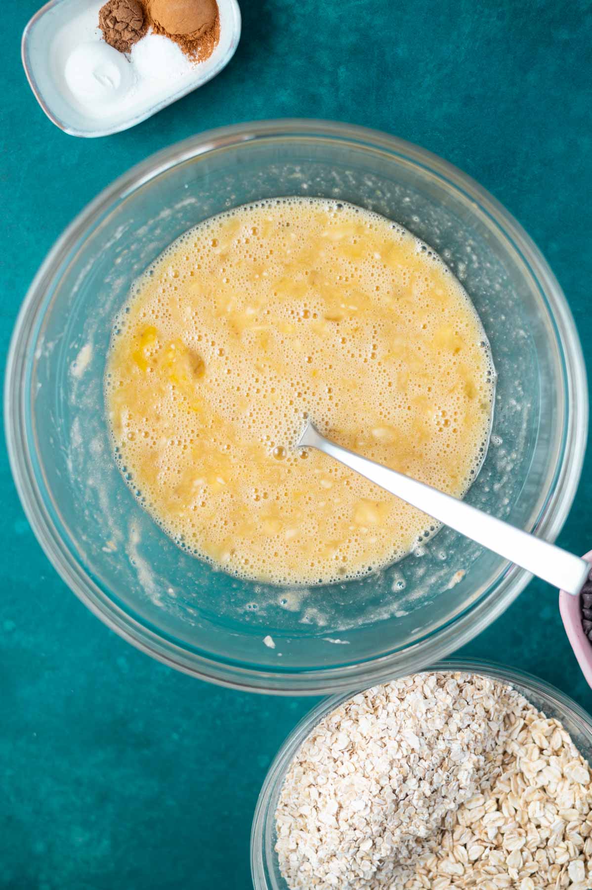 mashed banana, maple syrup, eggs and vanilla in a glass mixing bowl with a fork